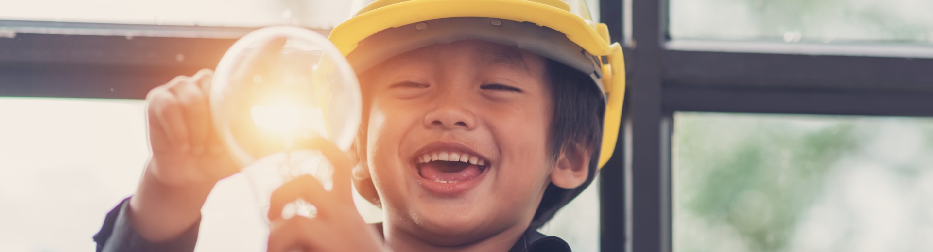 A child wearing a safety helmet holds a light bulb. A child wearing a safety helmet holds a light bulb.