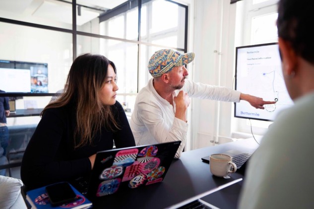 Equipo de trabajo en reunión de oficina analizando gráficos en pantalla y datos de proyecto en portátil.