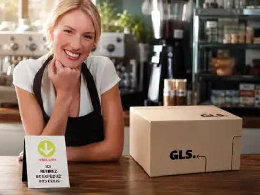 Commerçante souriante dans un point relais avec un colis GLS sur le comptoir.