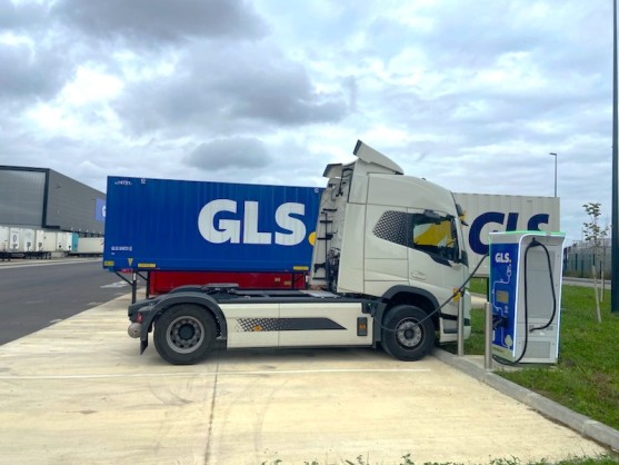 Camion tracteur électrique GLS en recharge sur une borne, devant un conteneur GLS sur un site logistique.