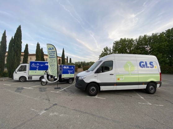 Flotte de véhicules de livraison électriques GLS : camionnette, triporteur et utilitaire, avec banderole « GLS s'engage pour un avenir meilleur ».