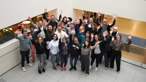 Groupe de collaborateurs GLS souriants et diversifiés, saluant la caméra dans un hall de bureaux moderne.