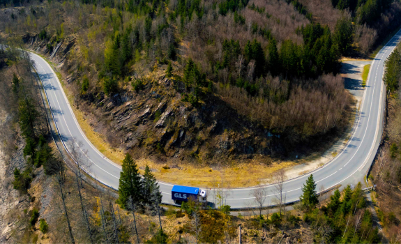 Camion semi-remorque GLS bleu sur une route de montagne en lacet, en milieu naturel.