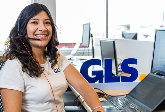 A GLS customer service agent smiling at the camera while sitting in front of her computer.